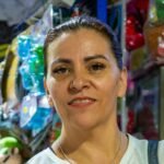 Smiling woman in market stall selling colorful toys in Ciudad de México.